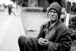 black and white picture of an older man sitting on a sidewalk
