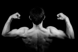 black and white picture of the back of a man with his arms up showing off muscles