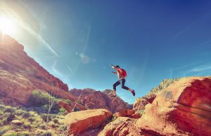 woman jumping from one rick to another while hiking