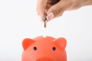 persons hand putting a coin into a piggy bank