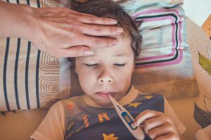 child laying in bed with a thermometer in his mouth