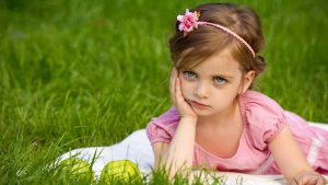 little girl sitting in the grass bored with hand on her chin