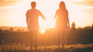 couple holding hands with a sunset in front of them