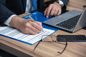 person signing paperwork next to a laptop
