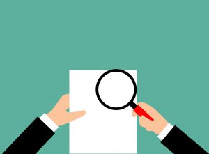hands looking at paper with magnifying glass