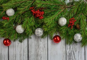 green tree branches with red and white holiday ornaments on top of a wooden background