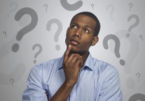 man shown thinking with his finger on his chin with question marks around his head