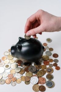 hand putting coins into a black piggy bank with coins surrounding the piggy bank