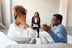 picture of a couple in a therapist session the woman is covering her ears while the man is talking