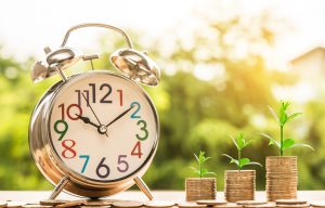 image of a clock next to piles of coins with sprouts growing on them